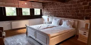 Das Bild zeigt ein Doppelzimmer mit Doppelbett und Steinfassade im Hoeferlhoft Wengelsbach im Elsass.